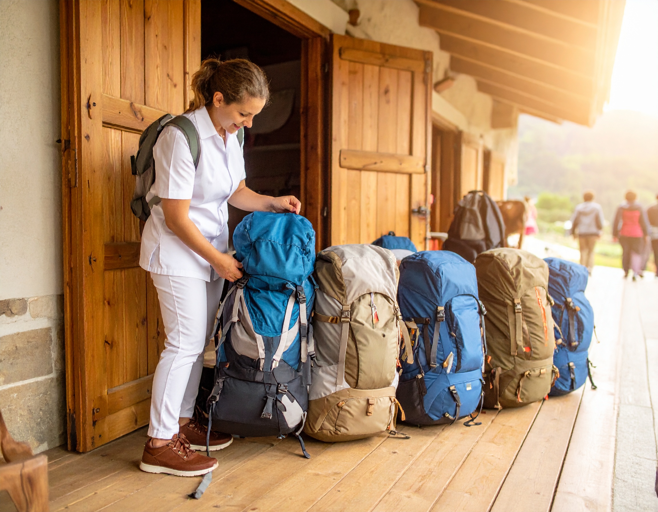 Group of diverse pilgrims smiling and standing next to their delivered backpacks at the entrance of a stone hostel on the Portuguese Camino during warm late afternoon light