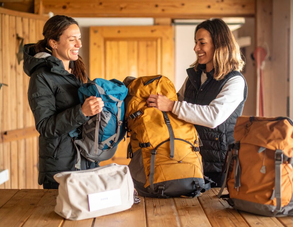 Two smiling pilgrims receive their backpacks at an accommodation at the end of a stage of the Camino de Santiago, showing joy and relief.